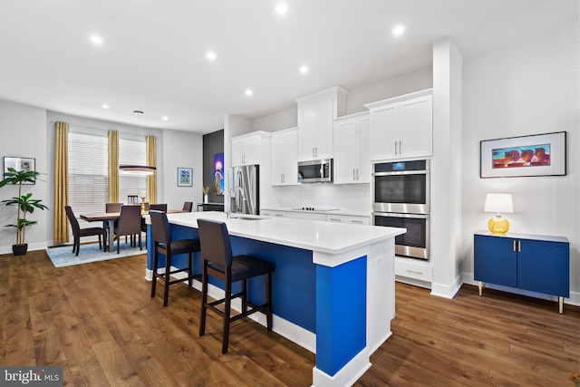 kitchen with a breakfast bar area, a kitchen island with sink, stainless steel appliances, and dark hardwood / wood-style flooring