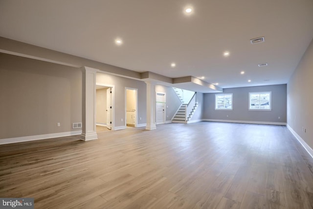 unfurnished living room featuring wood finished floors, visible vents, decorative columns, and stairs