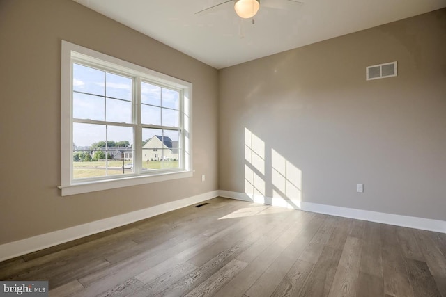 spare room with a ceiling fan, visible vents, baseboards, and wood finished floors