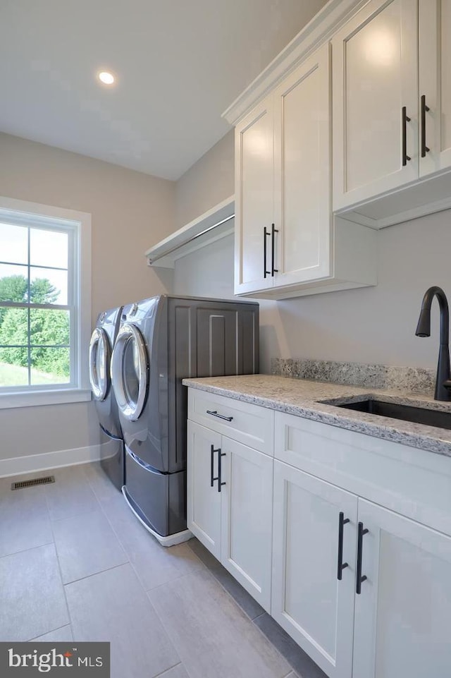 laundry area featuring light tile patterned floors, cabinet space, washing machine and dryer, a sink, and baseboards