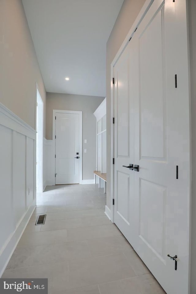 corridor featuring a wainscoted wall, visible vents, a decorative wall, and light tile patterned flooring