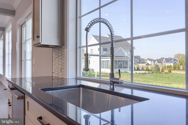 kitchen with a sink, white cabinets, stainless steel dishwasher, a residential view, and dark stone countertops