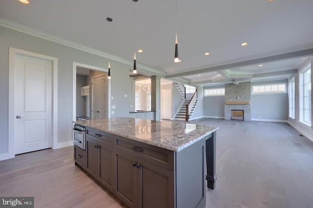 kitchen with light wood-style floors, a center island, a fireplace, and light stone counters