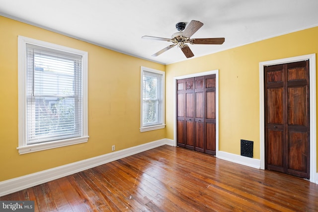 unfurnished bedroom featuring ceiling fan, wood-type flooring, and multiple windows