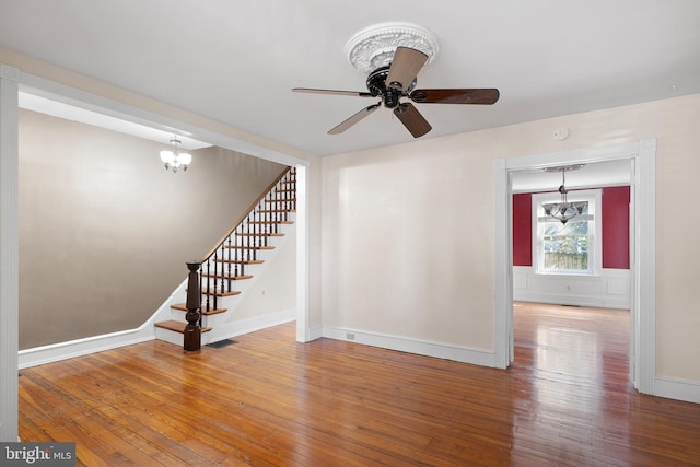 unfurnished living room featuring wood-type flooring and ceiling fan with notable chandelier