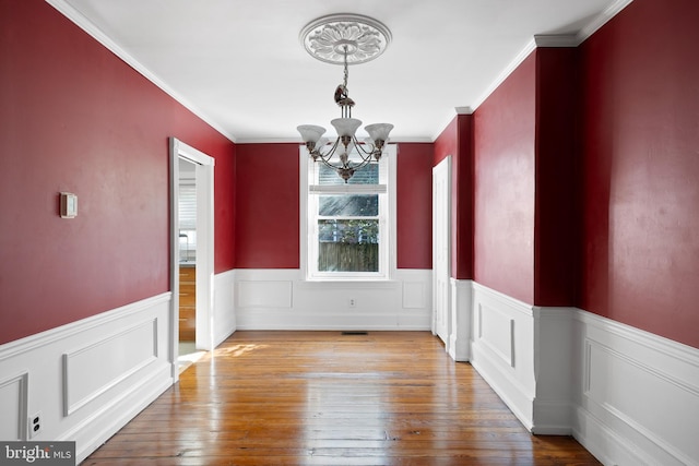 unfurnished dining area with crown molding, wood-type flooring, and a chandelier