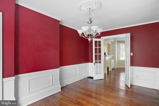 unfurnished dining area featuring french doors, crown molding, an inviting chandelier, and dark hardwood / wood-style floors