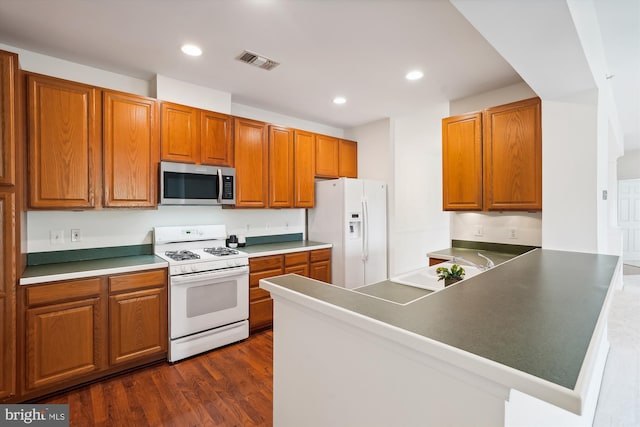 kitchen with white appliances, dark wood-type flooring, and kitchen peninsula