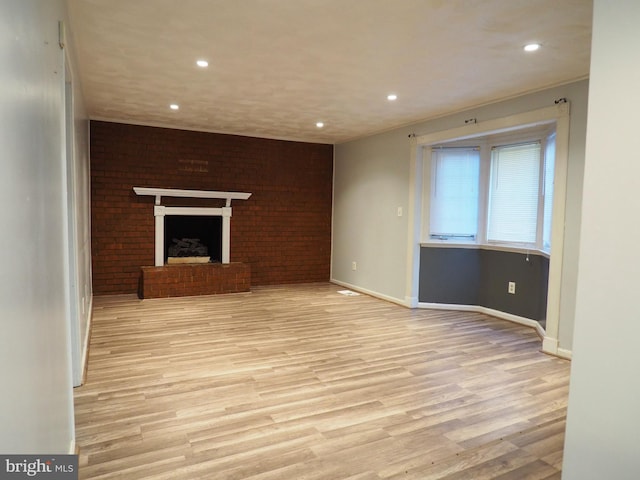 unfurnished living room featuring light hardwood / wood-style flooring, brick wall, and a brick fireplace