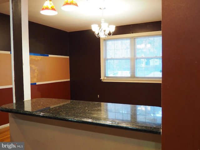 kitchen with dark stone countertops, a chandelier, hardwood / wood-style floors, and pendant lighting