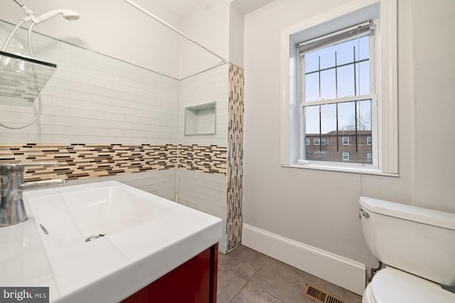 bathroom with toilet, vanity, tile patterned floors, and tiled shower