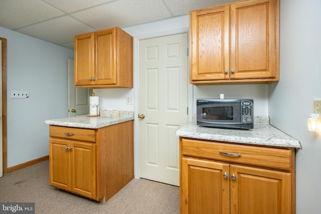 kitchen with light stone countertops, a drop ceiling, and light colored carpet