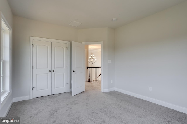 unfurnished bedroom with an inviting chandelier, light colored carpet, and a closet