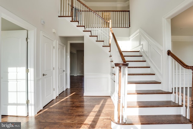 stairway with wood-type flooring and a towering ceiling