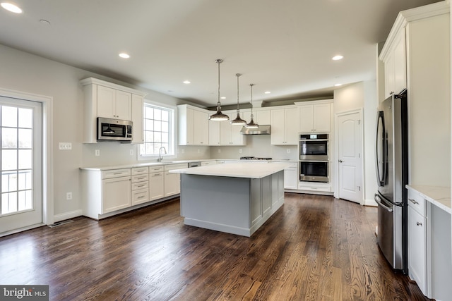 kitchen with dark wood-type flooring, appliances with stainless steel finishes, decorative light fixtures, and white cabinetry