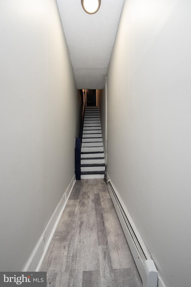 stairs featuring a textured ceiling, wood-type flooring, and baseboard heating