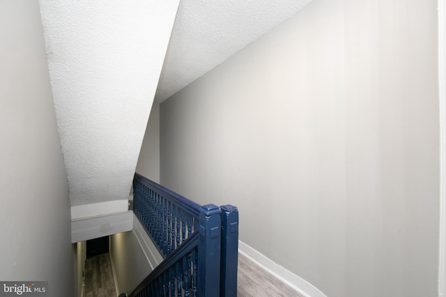 stairway with hardwood / wood-style floors, a textured ceiling, and lofted ceiling