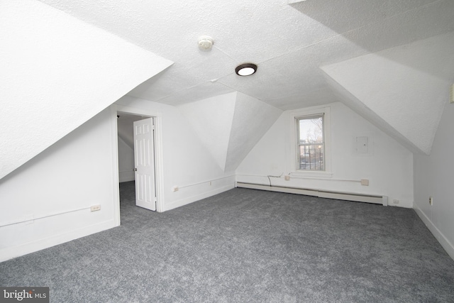 additional living space featuring a textured ceiling, dark colored carpet, lofted ceiling, and a baseboard heating unit