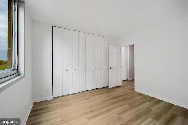 unfurnished bedroom with baseboards, light wood finished floors, and a closet