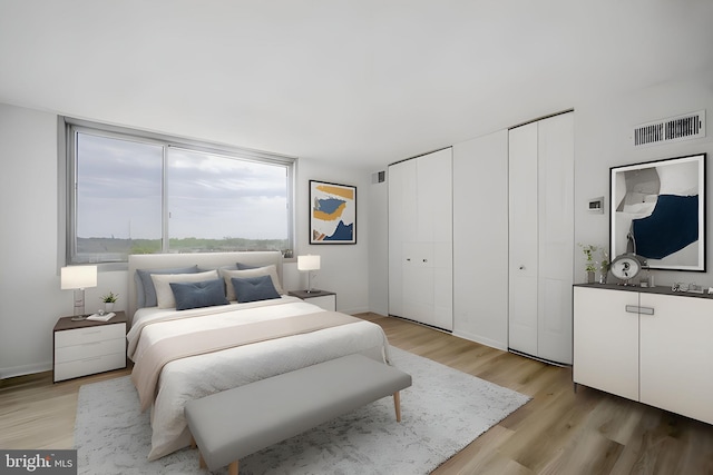 bedroom with visible vents, baseboards, light wood-style floors, and two closets