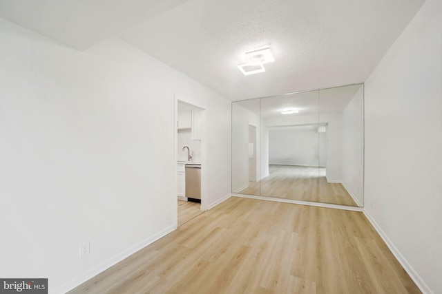 hall featuring a textured ceiling, baseboards, and light wood-style flooring