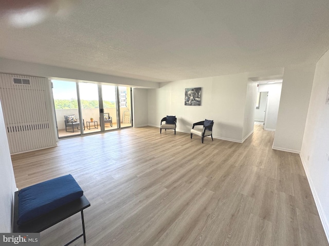 living area featuring visible vents, a textured ceiling, baseboards, and wood finished floors