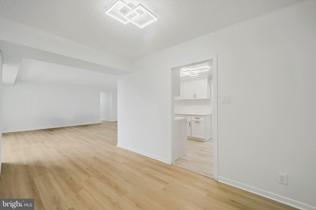additional living space featuring baseboards, a textured ceiling, light wood-style flooring, and visible vents