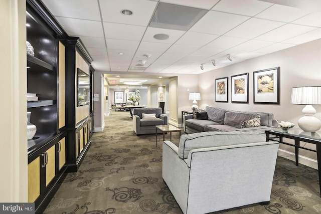 living area featuring baseboards, a drop ceiling, and dark colored carpet