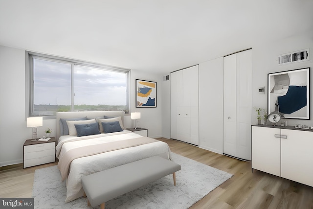 bedroom featuring visible vents, multiple closets, baseboards, and light wood-type flooring