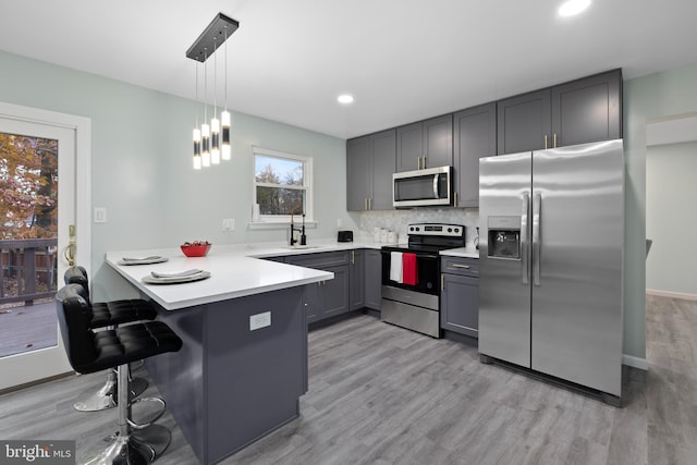 kitchen with appliances with stainless steel finishes, decorative light fixtures, sink, light hardwood / wood-style floors, and kitchen peninsula