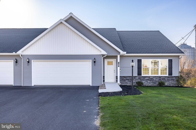 view of front of home featuring aphalt driveway, roof with shingles, a garage, and a front yard