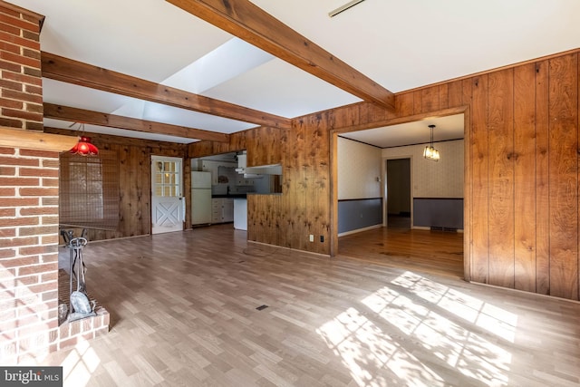 unfurnished living room featuring light wood-type flooring, wood walls, and beam ceiling