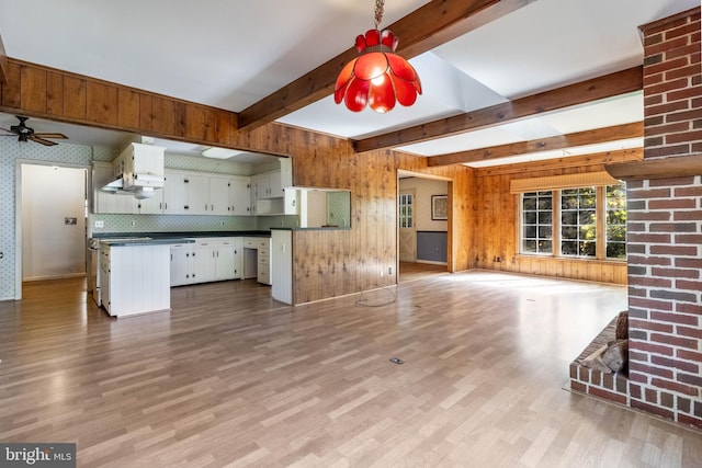 kitchen featuring tasteful backsplash, white cabinetry, beam ceiling, wooden walls, and light hardwood / wood-style flooring