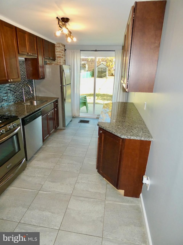 kitchen featuring decorative backsplash, light tile patterned floors, appliances with stainless steel finishes, stone counters, and sink