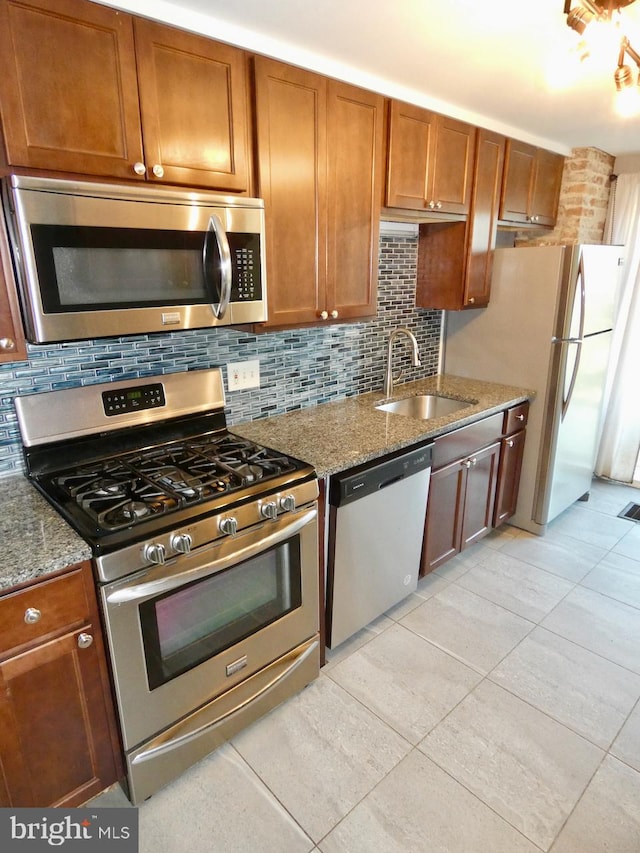 kitchen with tasteful backsplash, light stone counters, light tile patterned floors, appliances with stainless steel finishes, and sink