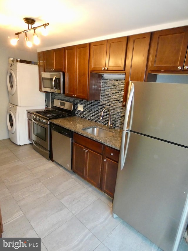 kitchen featuring stacked washer and clothes dryer, dark stone countertops, sink, appliances with stainless steel finishes, and tasteful backsplash