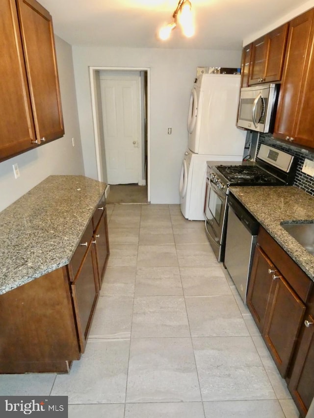 kitchen with tasteful backsplash, stacked washing maching and dryer, light stone countertops, light tile patterned flooring, and stainless steel appliances