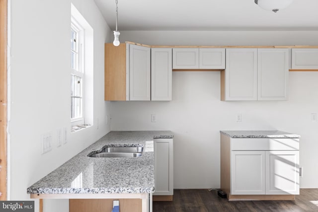 kitchen with pendant lighting, sink, white cabinets, light stone countertops, and dark wood-type flooring