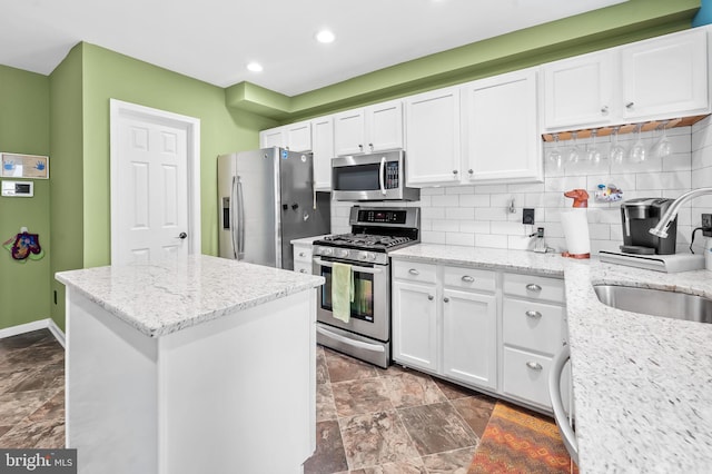 kitchen with stainless steel appliances, light stone counters, white cabinetry, and sink