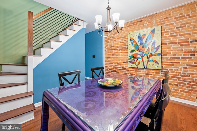 dining room with hardwood / wood-style floors, brick wall, and an inviting chandelier