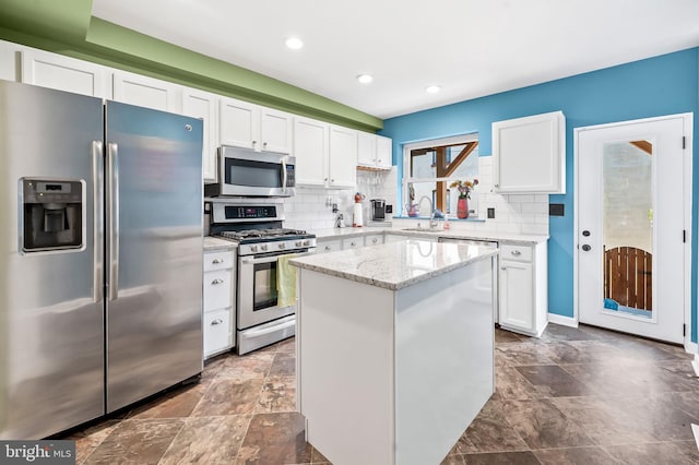 kitchen featuring light stone countertops, decorative backsplash, stainless steel appliances, white cabinetry, and a kitchen island