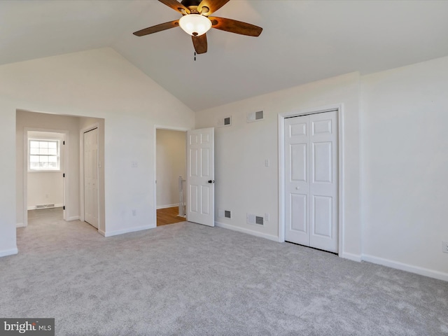 unfurnished bedroom with two closets, light colored carpet, high vaulted ceiling, and ceiling fan