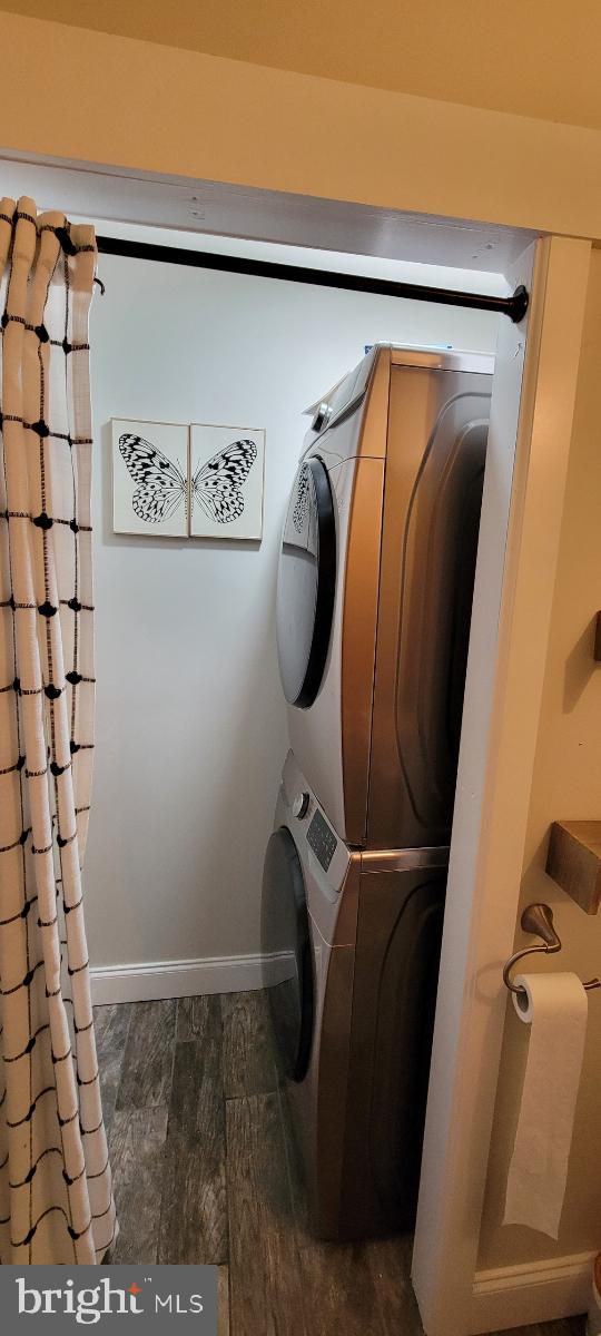 laundry room featuring stacked washing maching and dryer and dark hardwood / wood-style floors