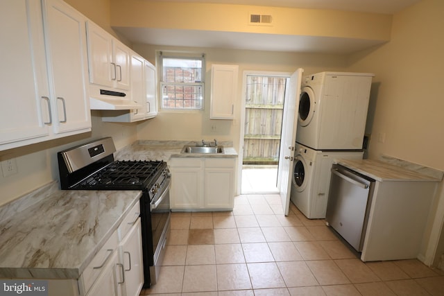 kitchen featuring white cabinets, light tile patterned floors, stacked washing maching and dryer, sink, and stainless steel appliances