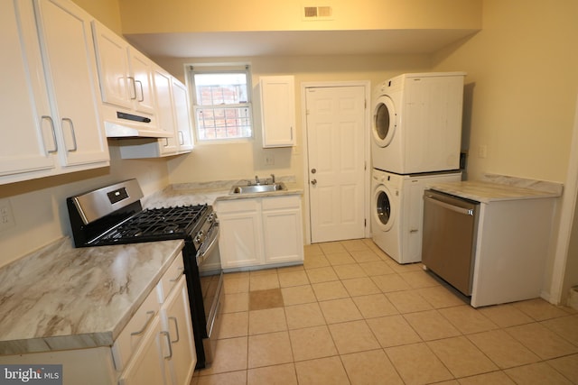 kitchen featuring stacked washing maching and dryer, stainless steel appliances, sink, light tile patterned floors, and white cabinets