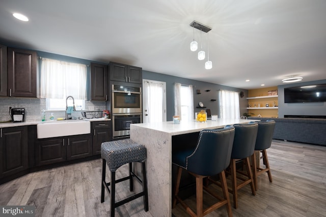 kitchen featuring a kitchen breakfast bar, light wood-type flooring, double oven, and sink