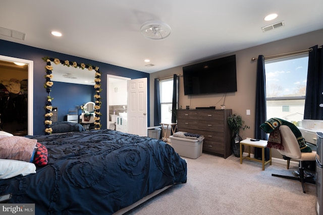 bedroom with light colored carpet, a walk in closet, and multiple windows