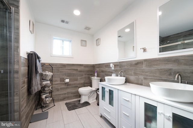 bathroom with a shower with door, vanity, tile walls, and toilet