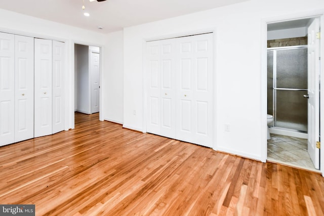 unfurnished bedroom with multiple closets, ensuite bathroom, and light wood-type flooring