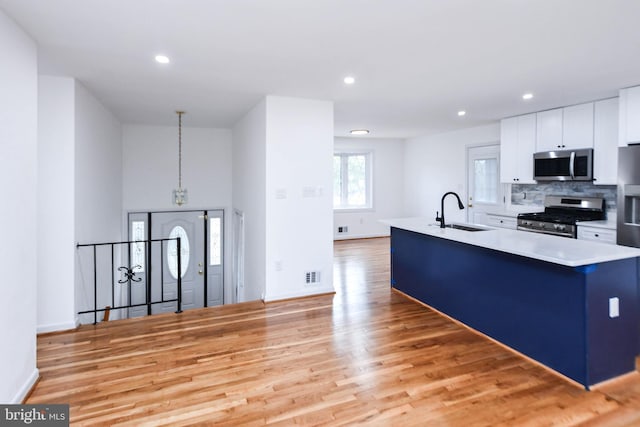 kitchen with an island with sink, appliances with stainless steel finishes, light wood-type flooring, sink, and decorative light fixtures